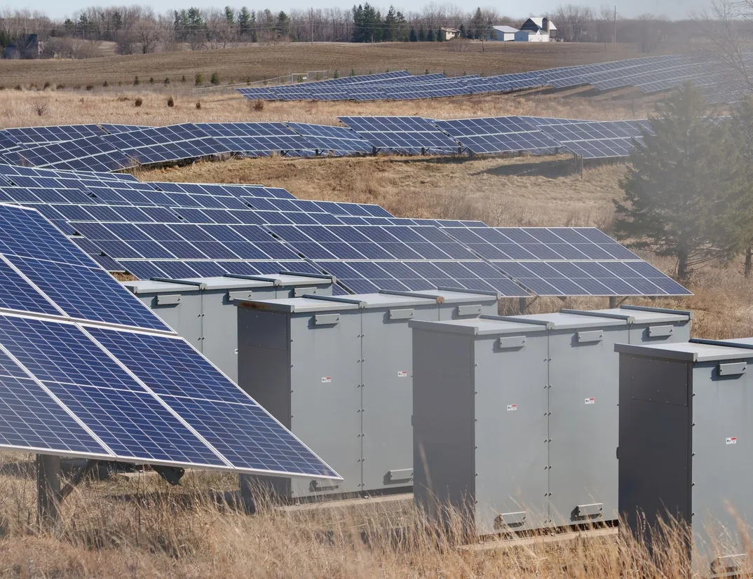 Rows of solar panels and battery storage units in a dry field