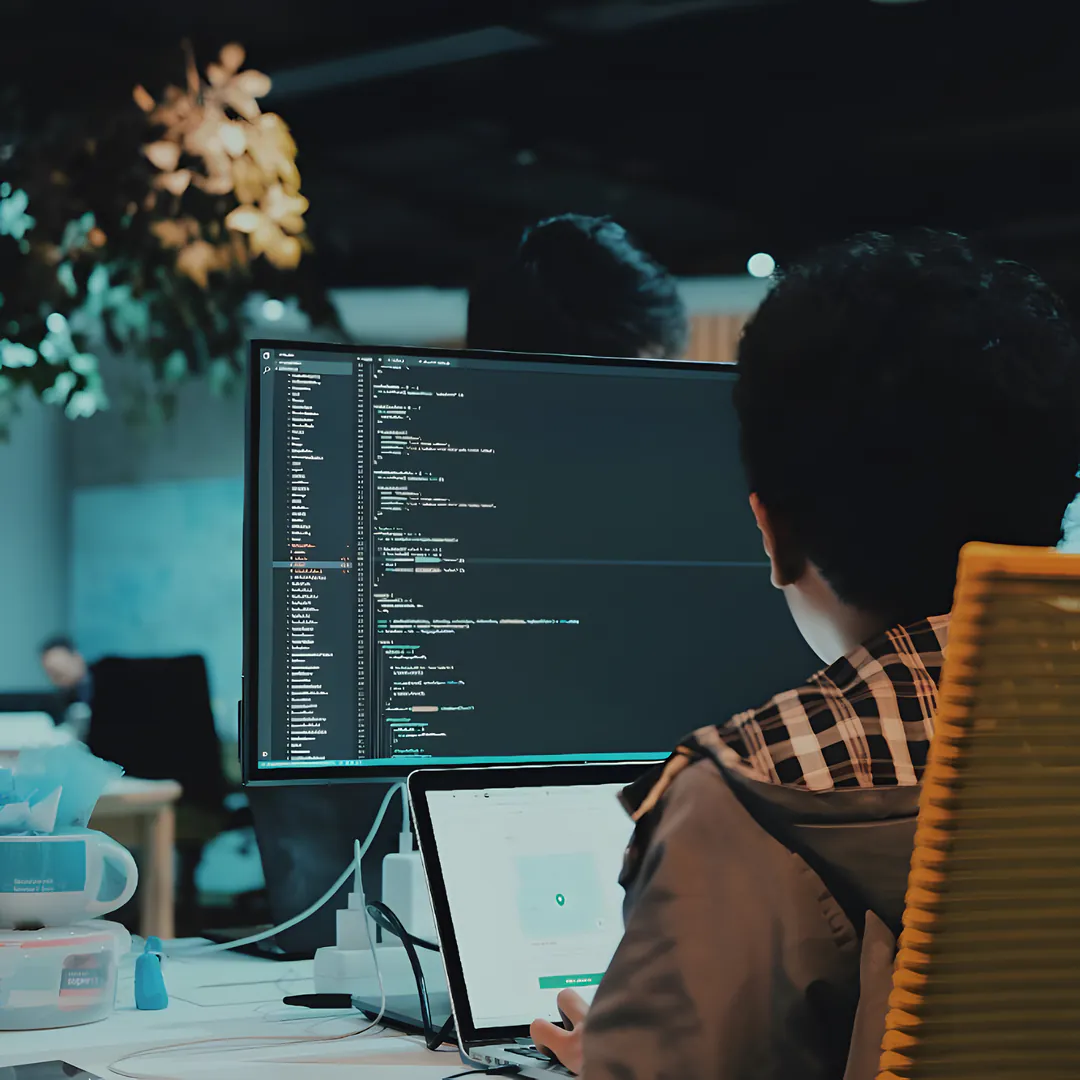 An engineer reviewing code on a monitor in an open office